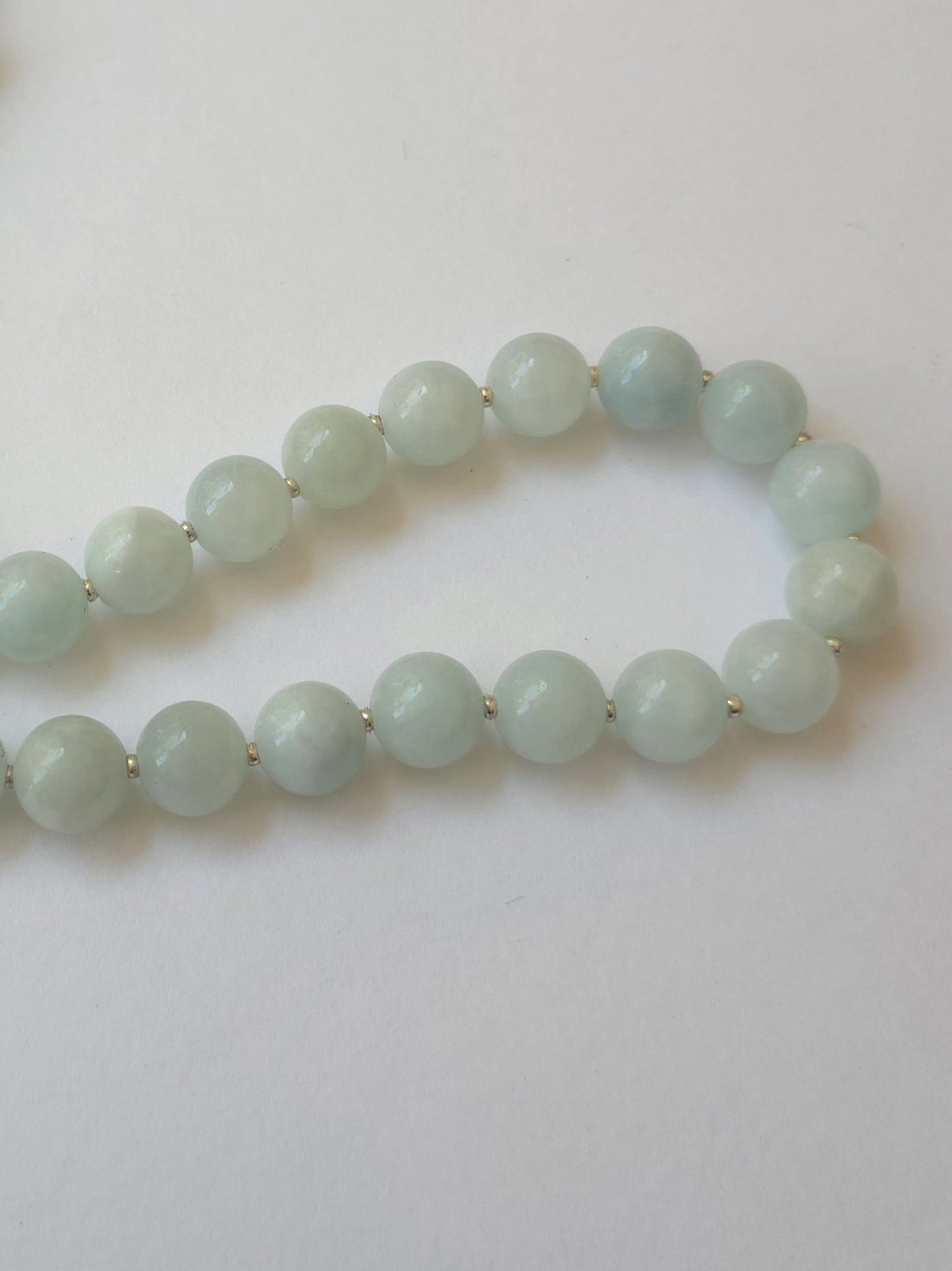 A strand of light green jade-like round beads with small silver spacer rings, arranged in a curved shape on a plain white background.