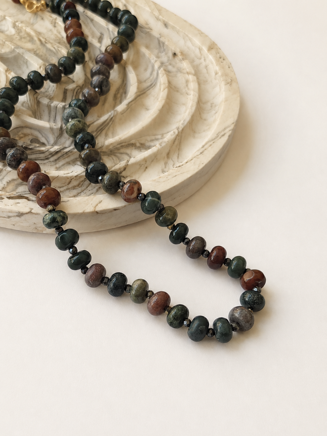 Indian agate necklace with pyrite accents styled beside a marbled neutral dish