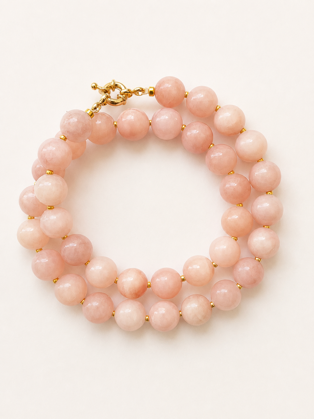 Blush pink jadeite necklace arranged in a soft coil, showing 10mm beads and golden details.