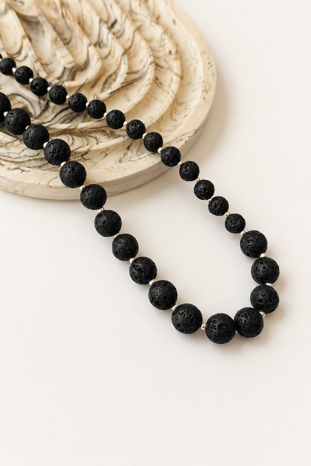 Graduated black lava stone necklace styled beside a marble dish on a neutral background