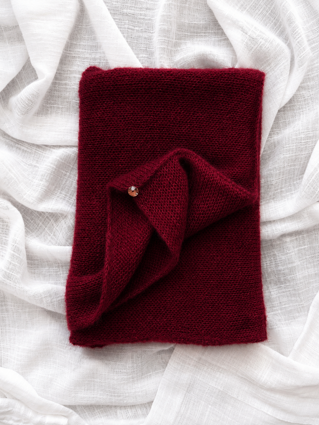 Folded burgundy infinity scarf on white linen fabric.