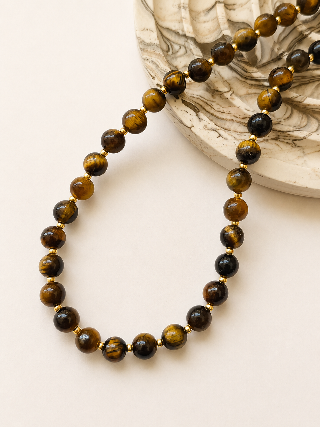 Tiger eye gemstone necklace styled beside a neutral marbled decorative object