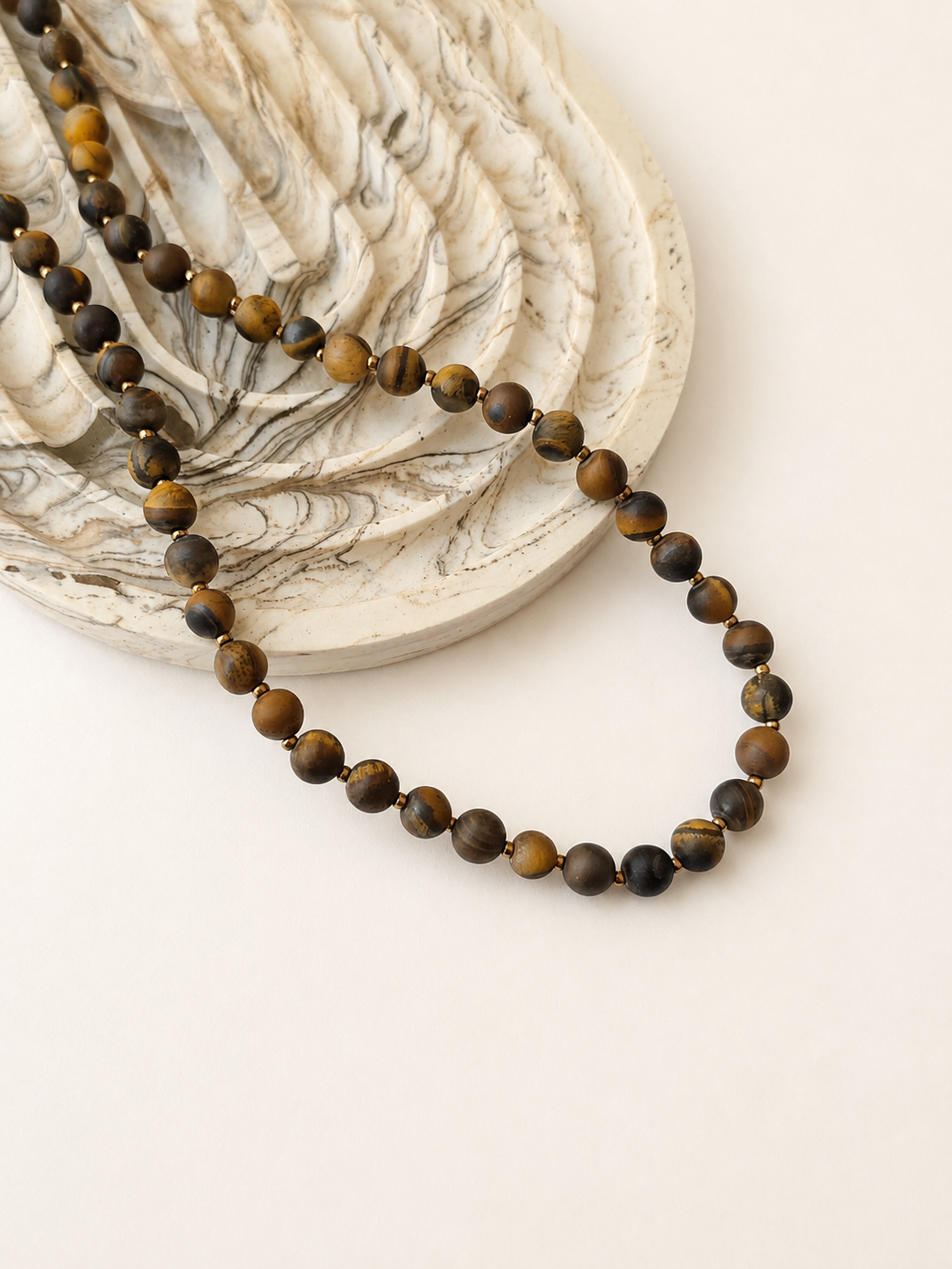 Matte tiger eye necklace styled beside a marbled neutral dish on a warm ivory background