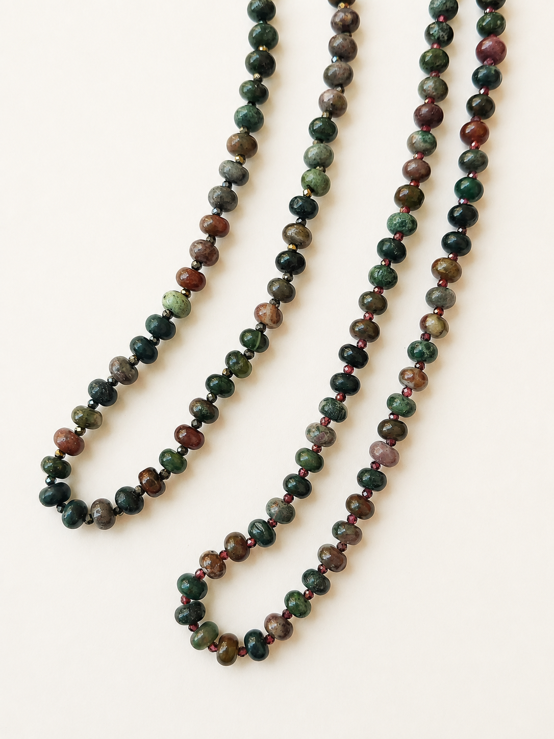 Two Indian agate necklaces with burgundy and pyrite accents displayed together on a warm ivory background
