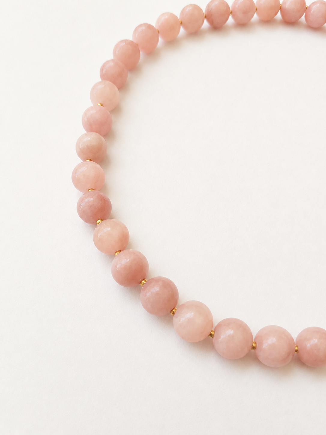 Close-up of blush pink jadeite gemstone beads with small Japanese Miyuki gold spacer beads.