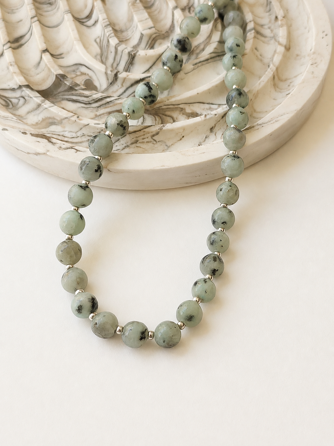 Kiwi jasper necklace with silver accents styled beside a marbled neutral dish