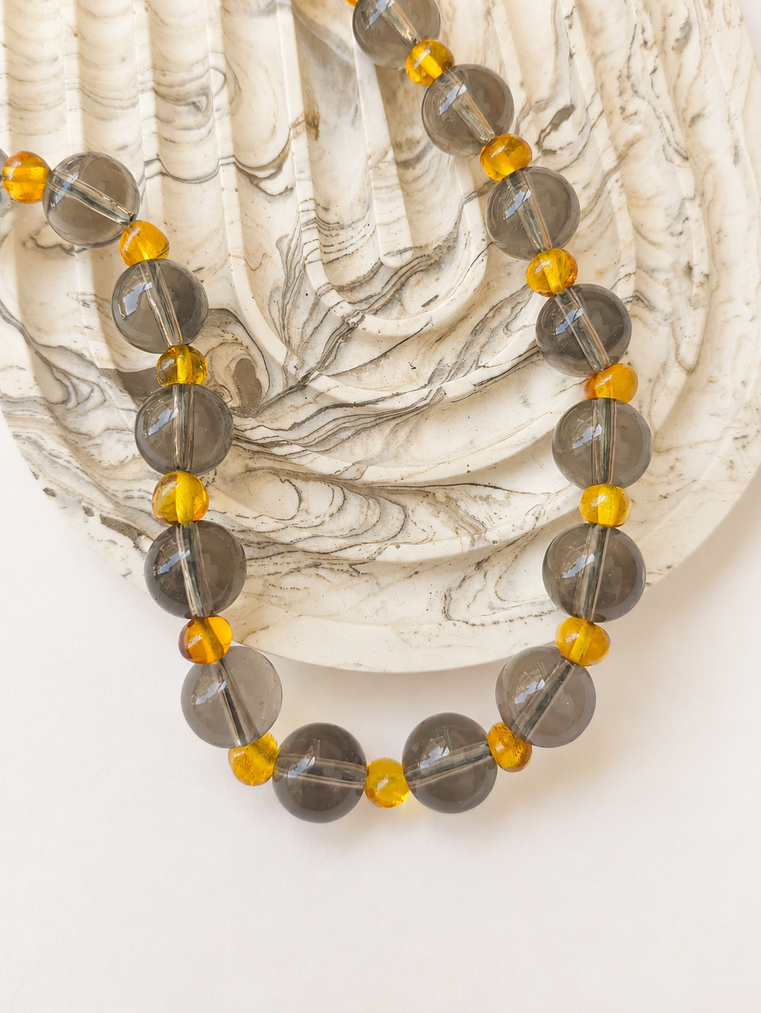 Smoky quartz and Baltic amber necklace styled beside a marbled decorative tray