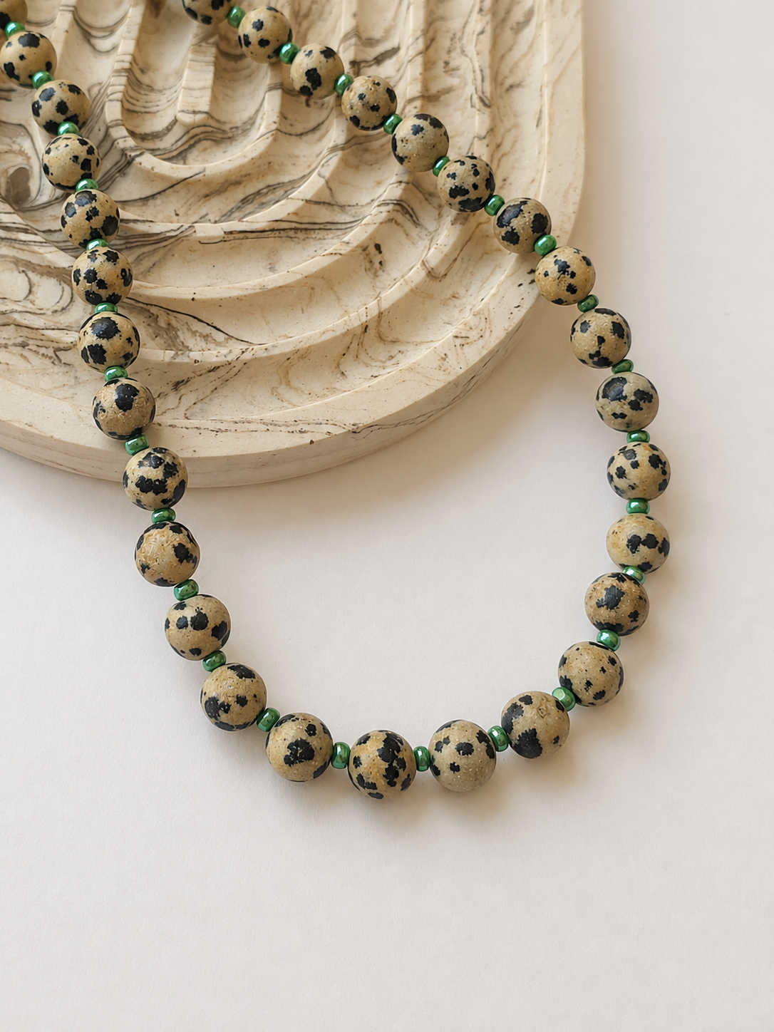 Dalmatian jasper necklace with green accents styled beside a marbled neutral dish