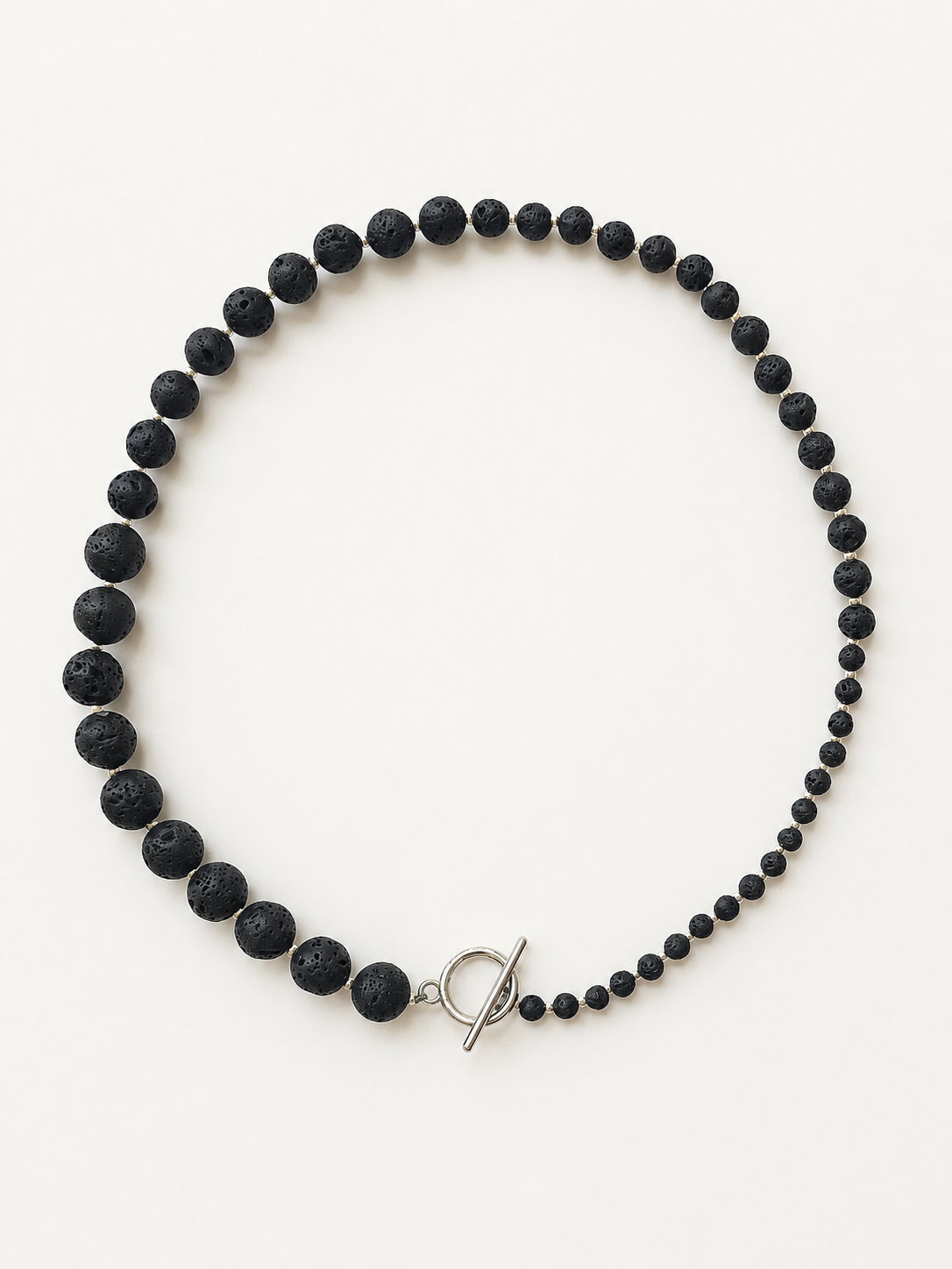 Graduated black lava stone necklace with silver accents and toggle clasp on a warm ivory background
