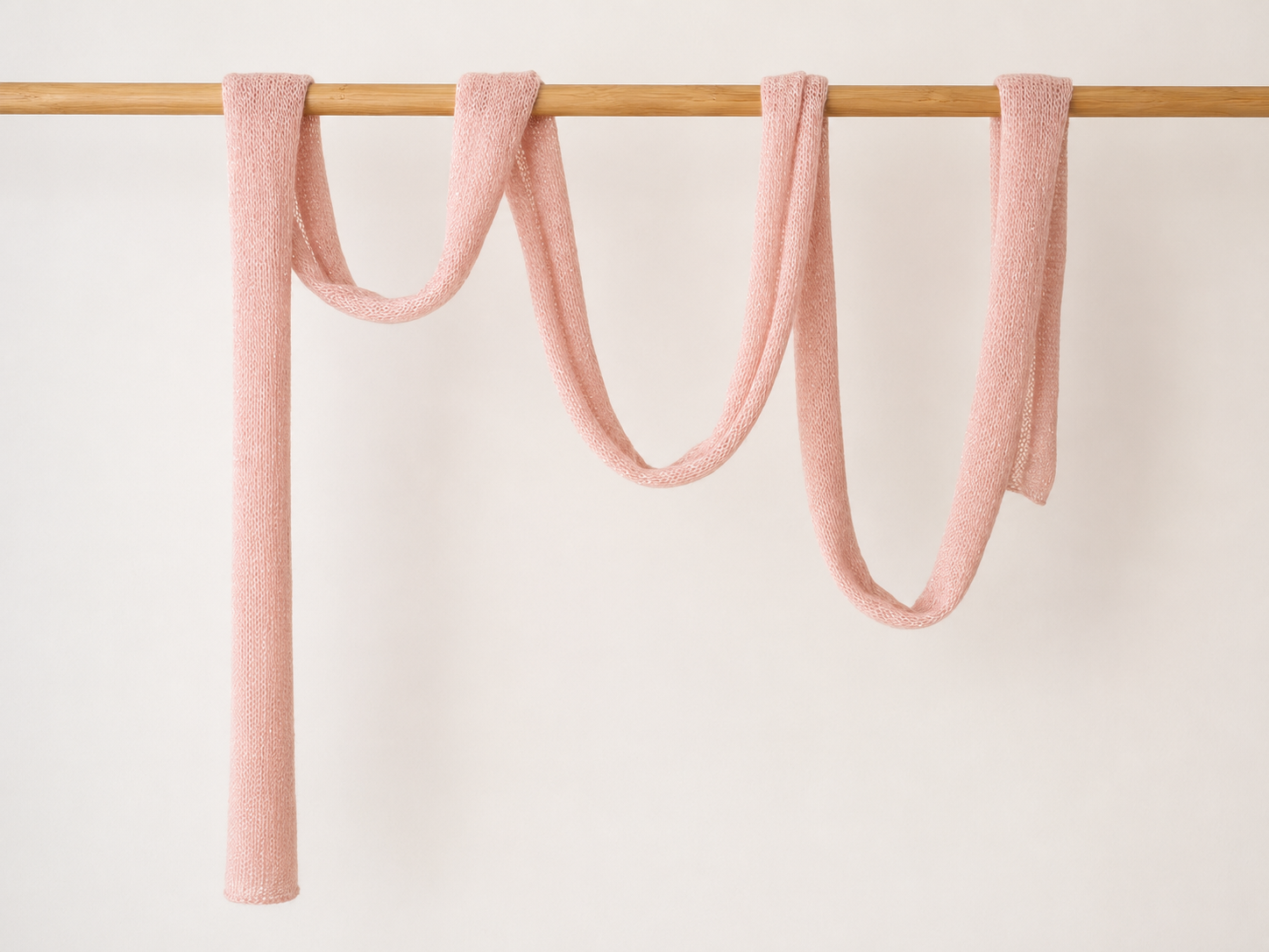 Extra long pink knitted scarf draped on clothing rail