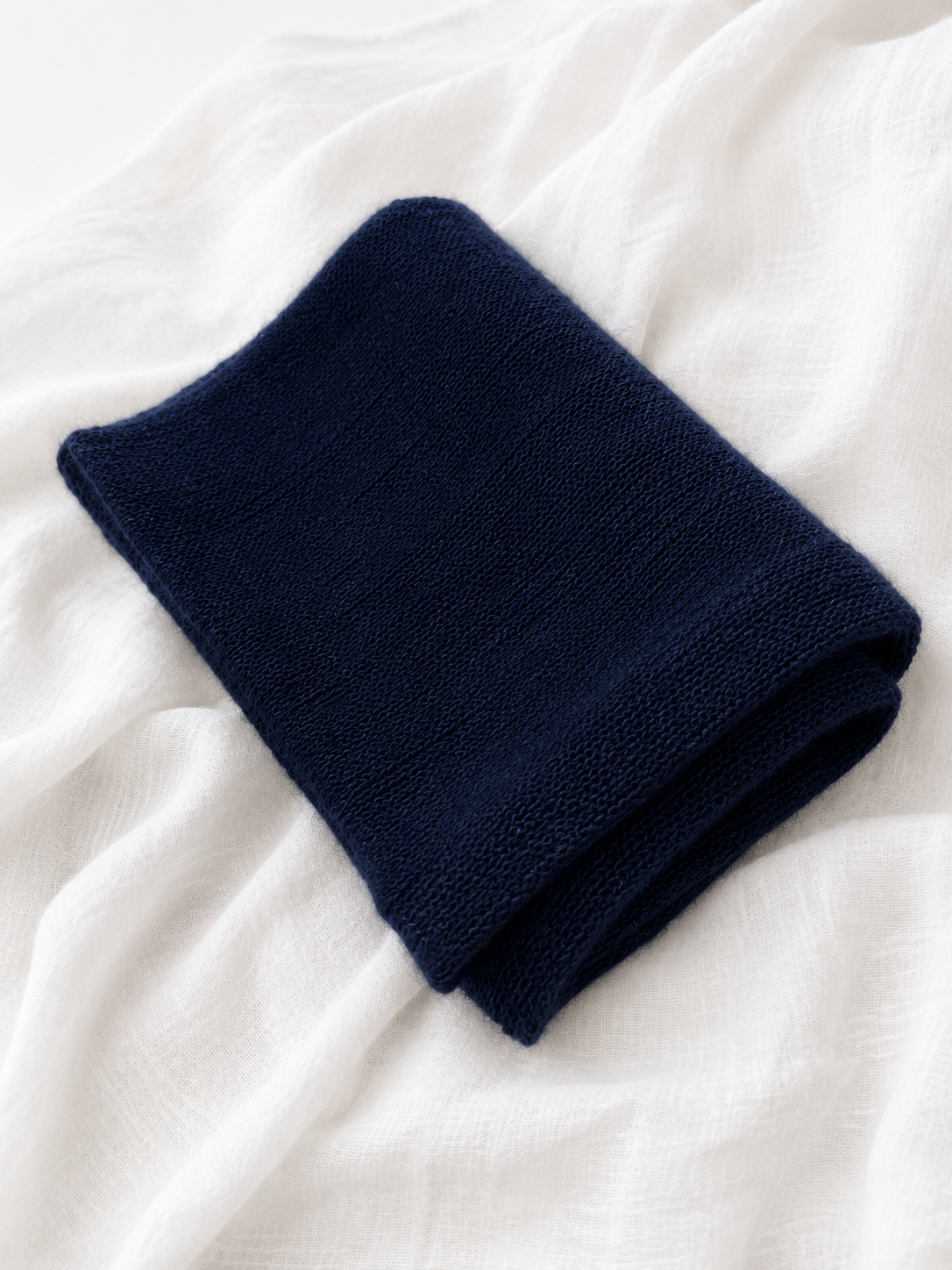 Folded midnight navy infinity scarf displayed on white linen fabric.