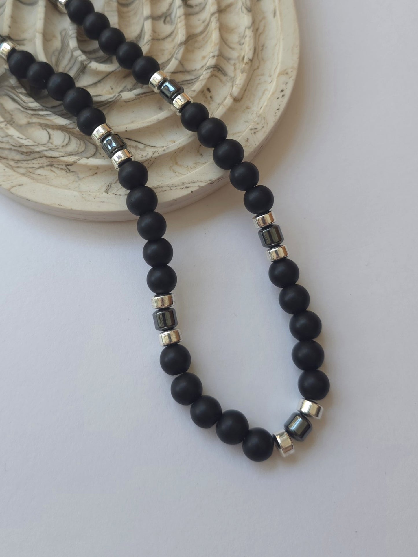 Matte black synthetic shungite necklace styled beside a marble dish on a neutral background