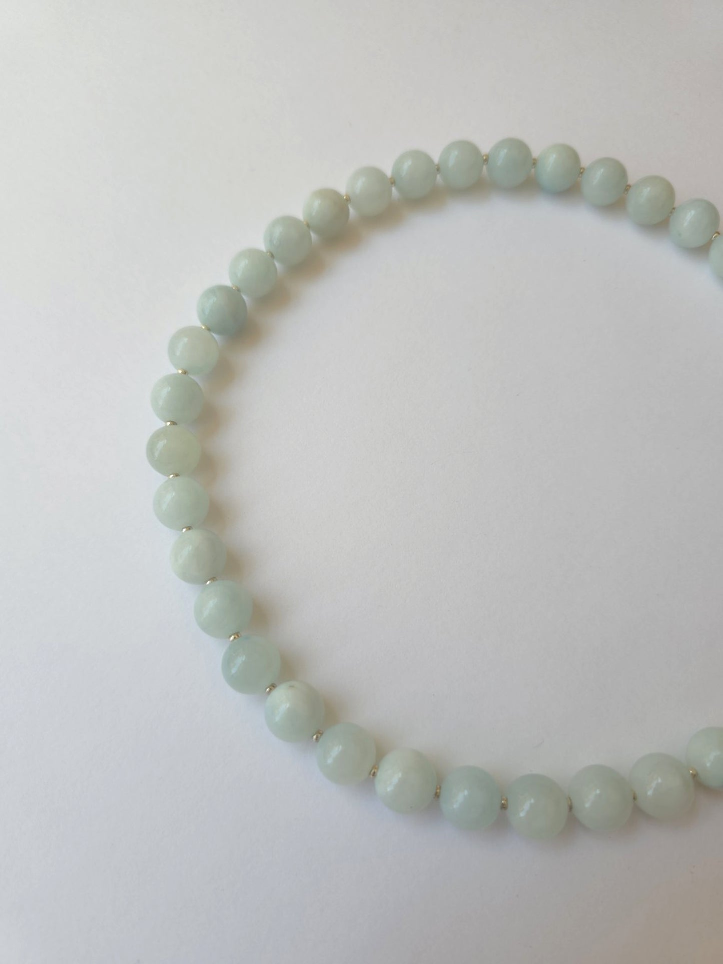 A beaded necklace made of pale mint jadeite green polished round beads, displayed on a plain white background.