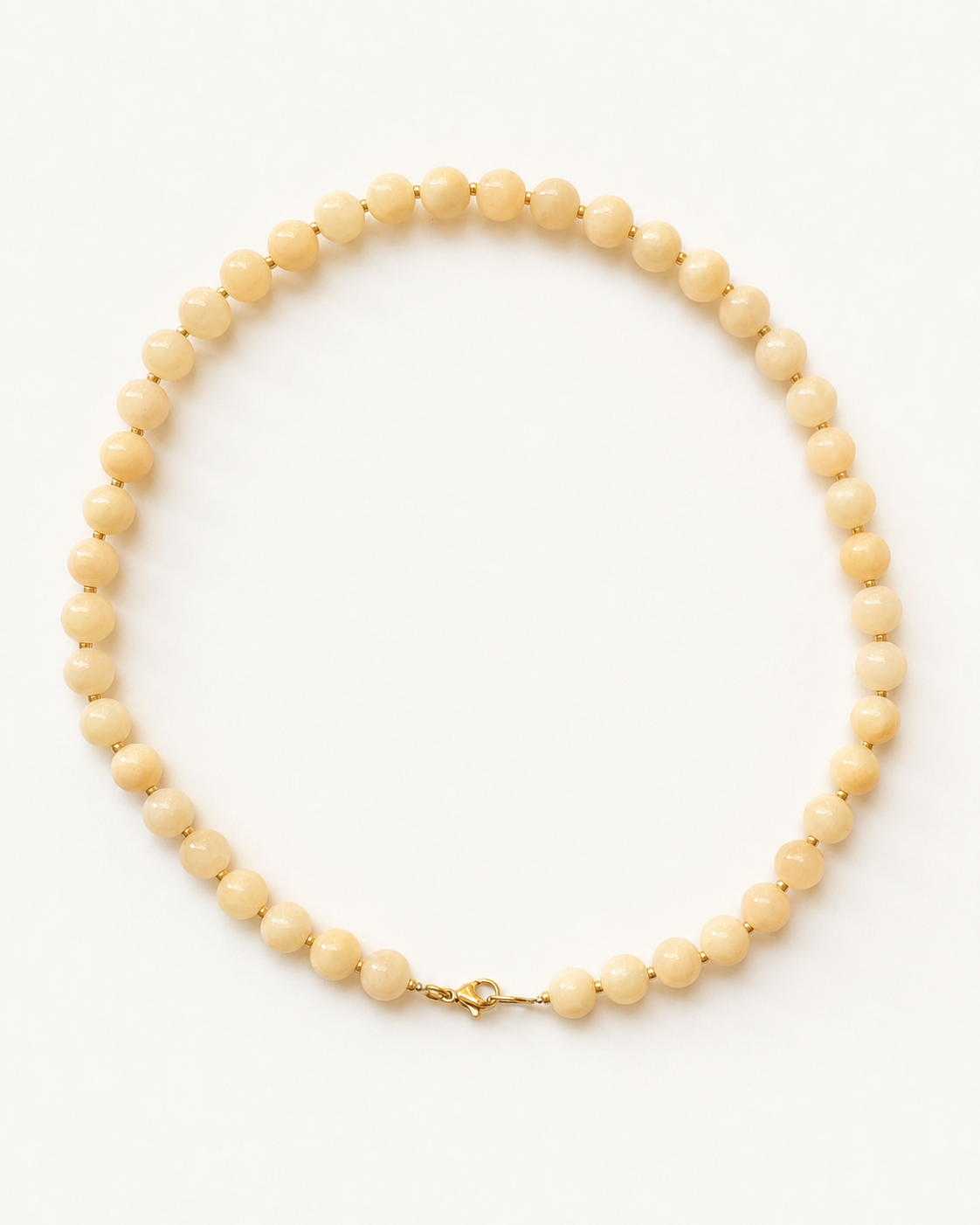 Light peach jadeite necklace with gold accents and lobster clasp on a warm ivory background