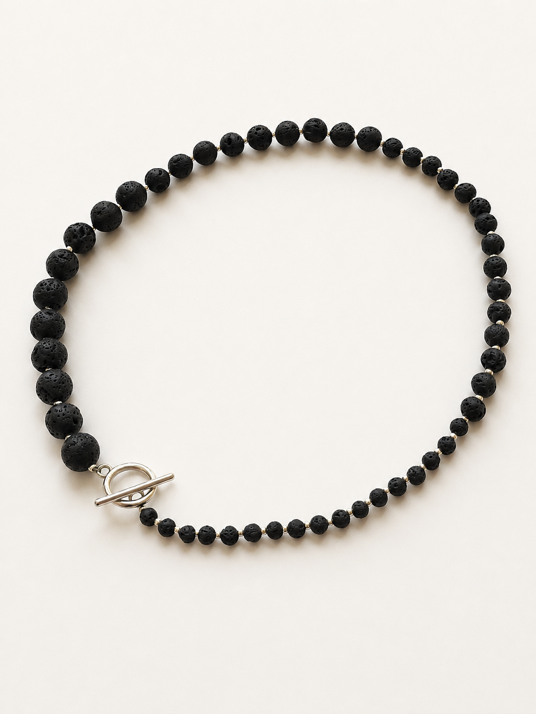 Graduated lava stone necklace arranged with stainless steel toggle clasp on a neutral background