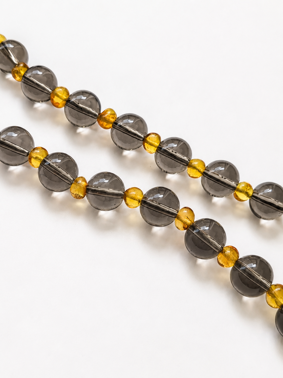 Close-up of polished smoky quartz beads separated by irregular golden Baltic amber beads