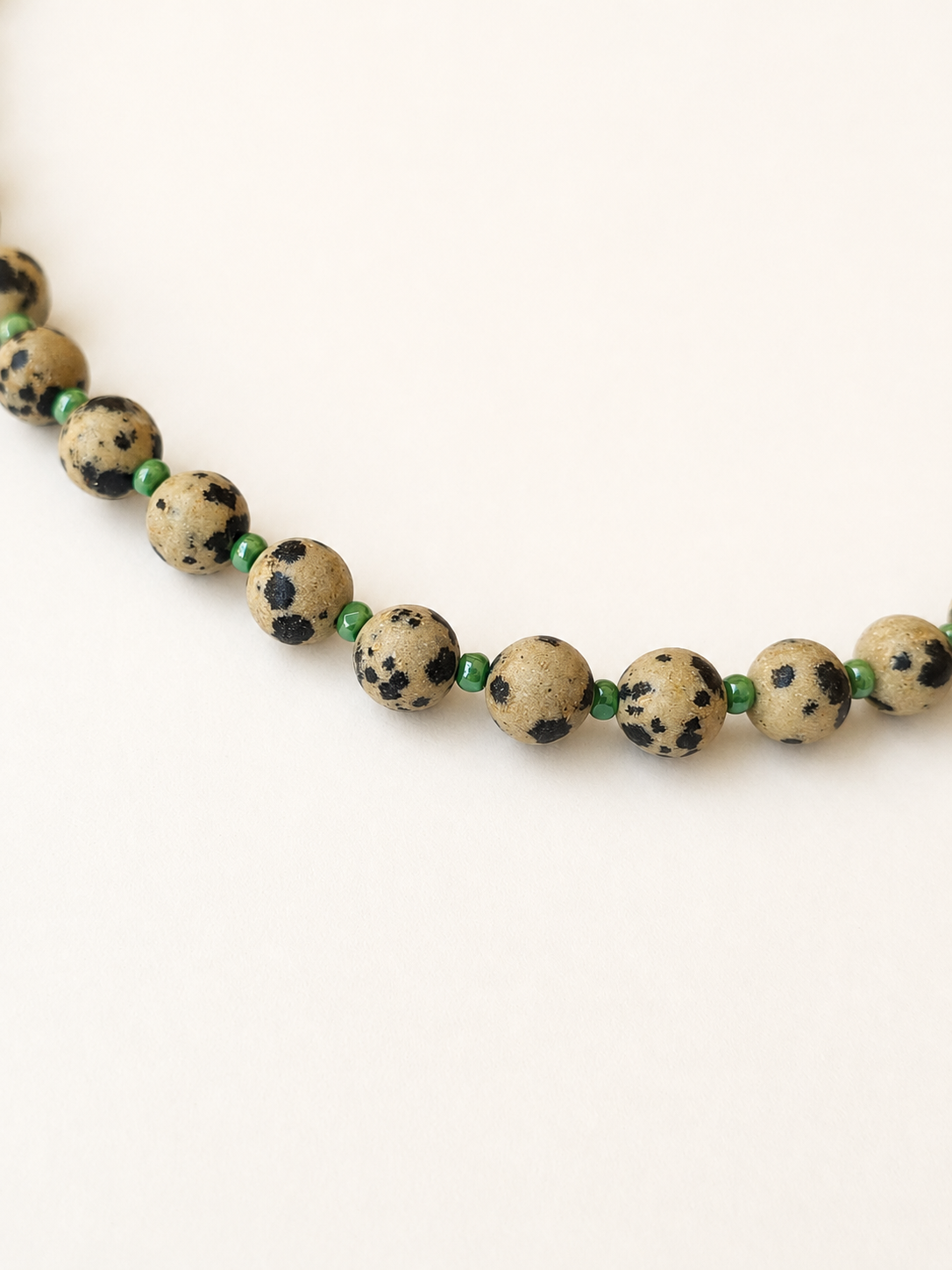Detailed view of beige and black spotted Dalmatian jasper beads with green accents