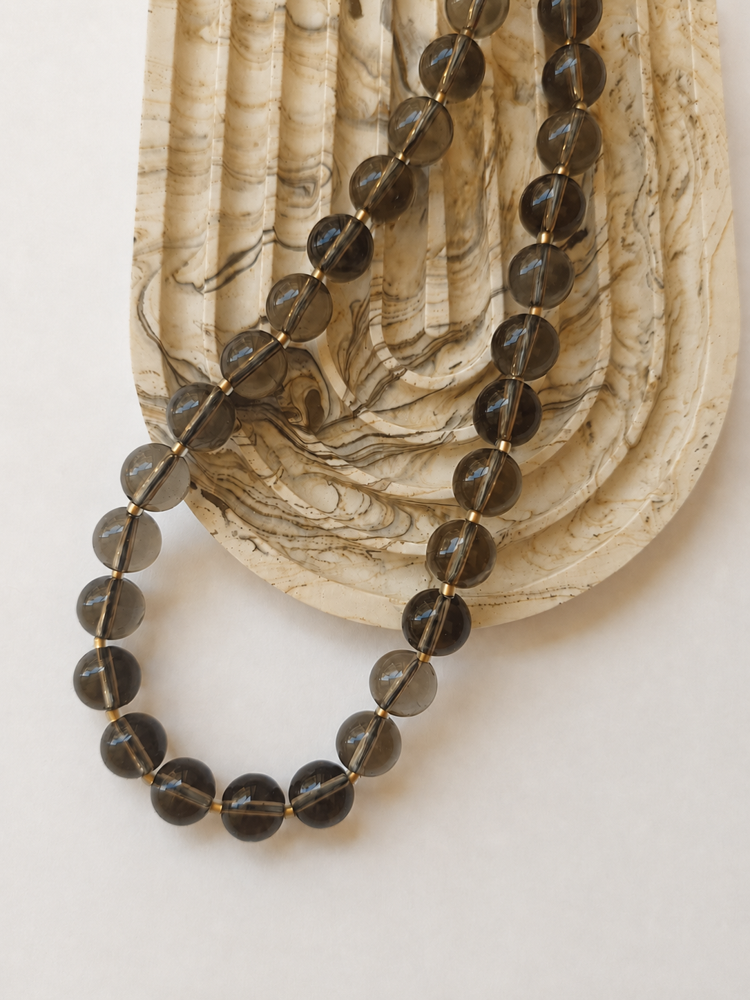 Smoky quartz necklace with large translucent beads styled beside a marble dish