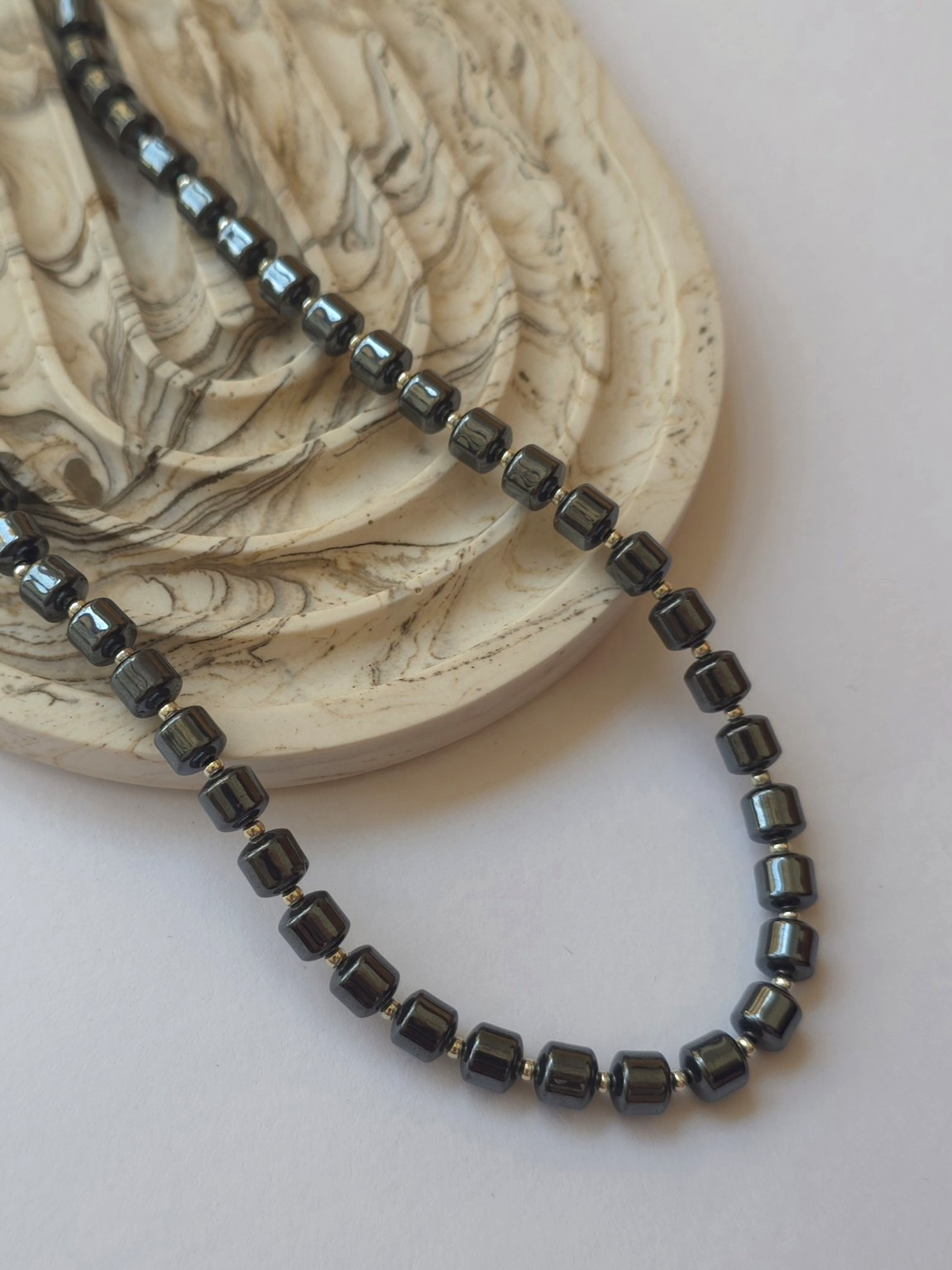 Hematite column necklace styled beside a marble dish on a neutral background