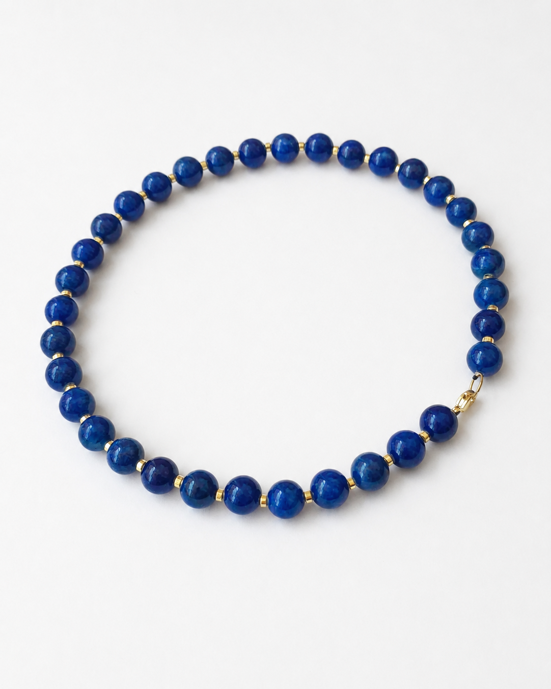 Angled full view of a vivid blue jadeite bead necklace with gold-coloured hematite accents