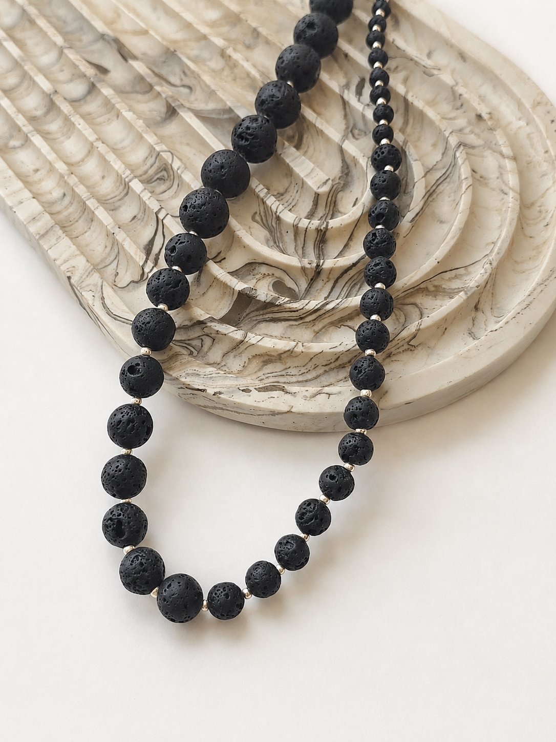 Black lava stone necklace styled beside a marble dish on a warm neutral background