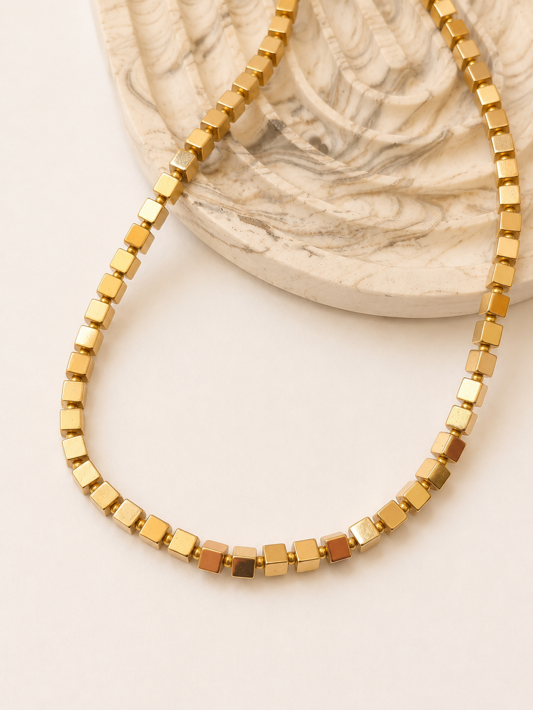 Gold hematite cube necklace styled beside a neutral marbled decorative object