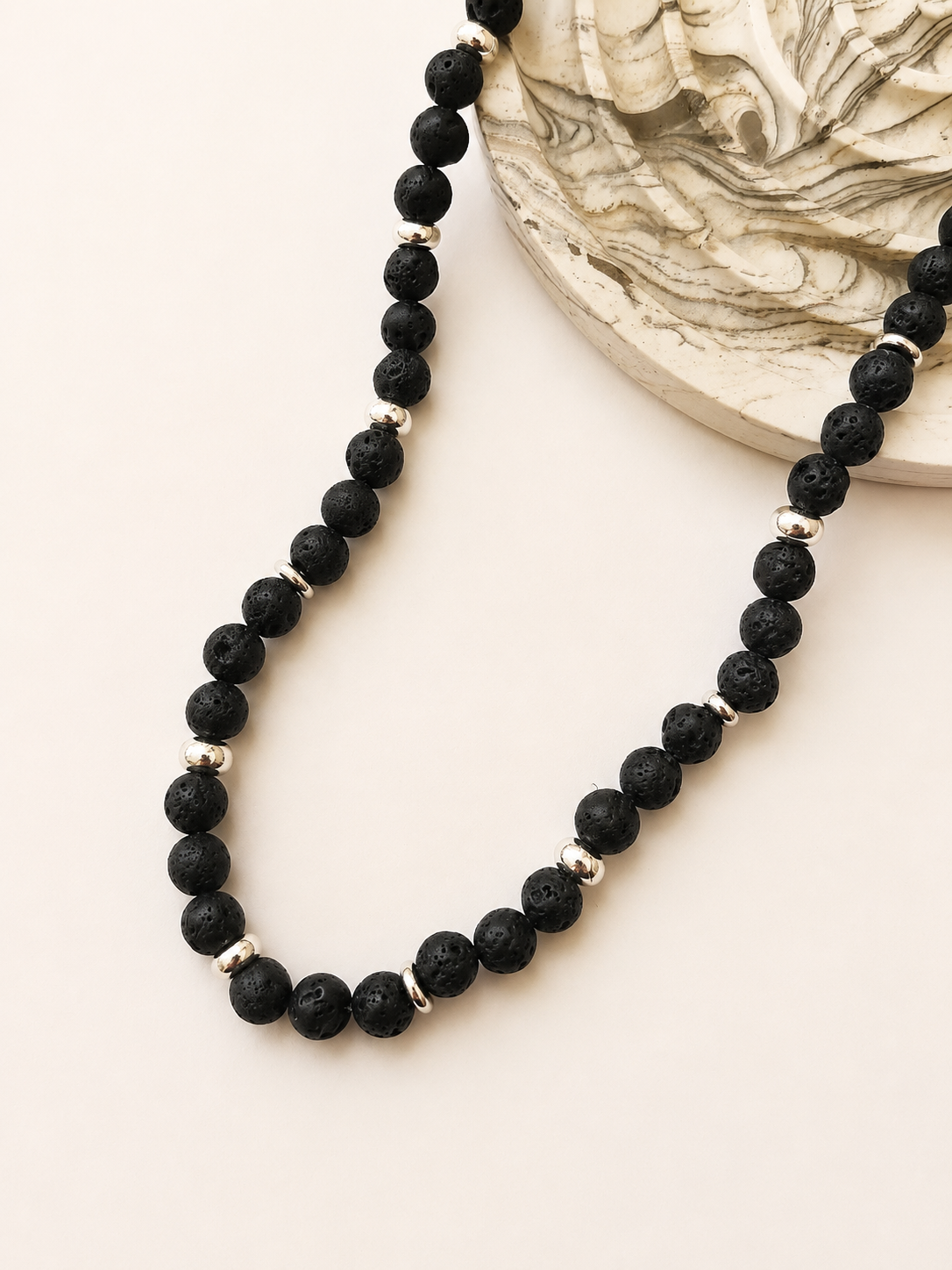 Black lava stone necklace styled beside a neutral marbled decorative object