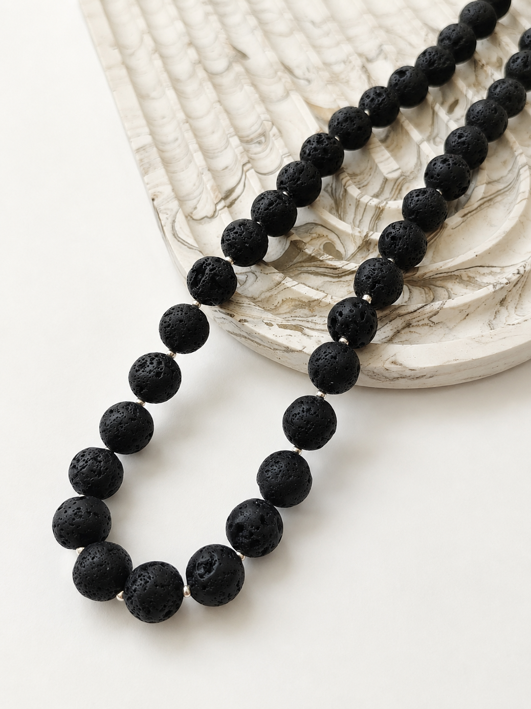 Black lava bead necklace styled beside a neutral marbled decorative object
