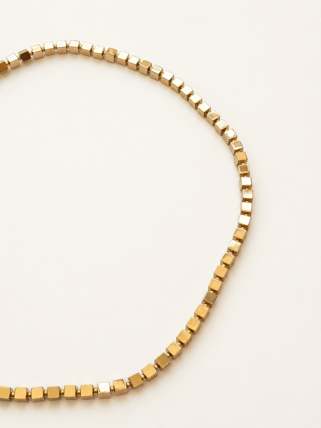 Close-up of reflective 4mm hematite cube beads separated by small gold Miyuki beads