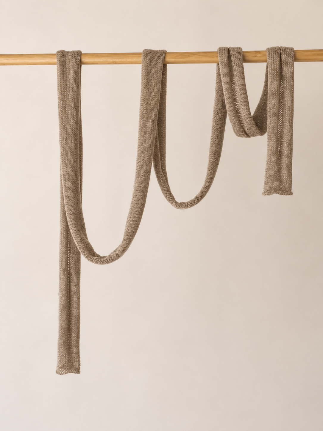 Extra long handmade skinny scarf draped on a wooden rail.