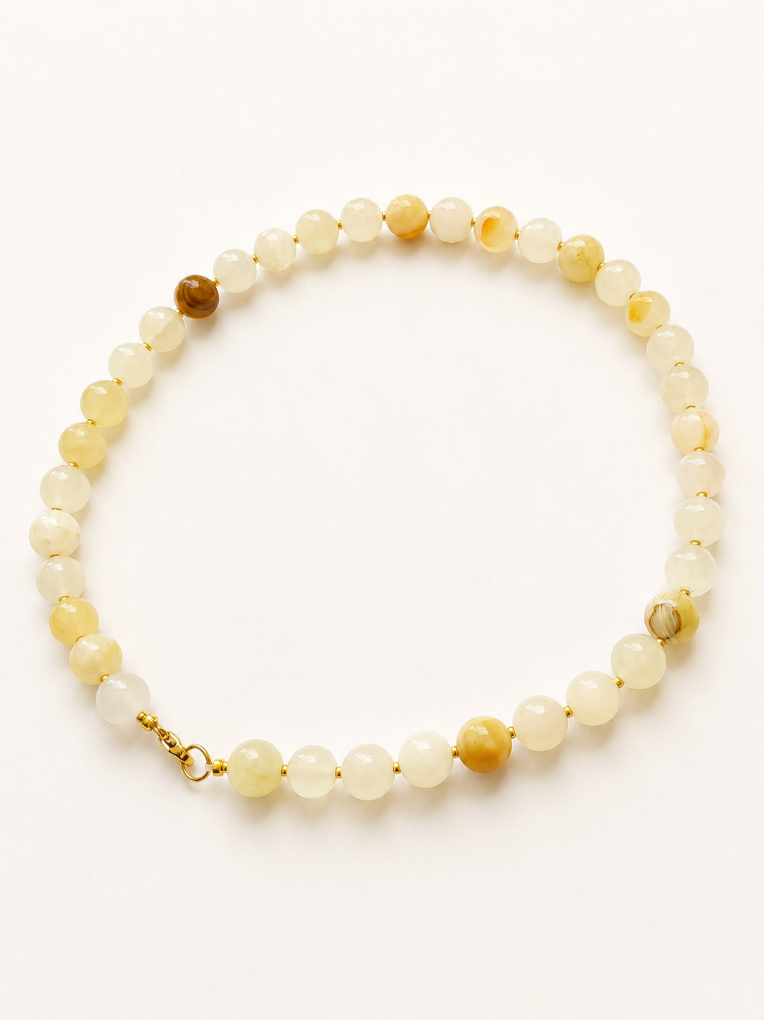Angled full view of a cream and pale yellow jadeite bead necklace with golden details