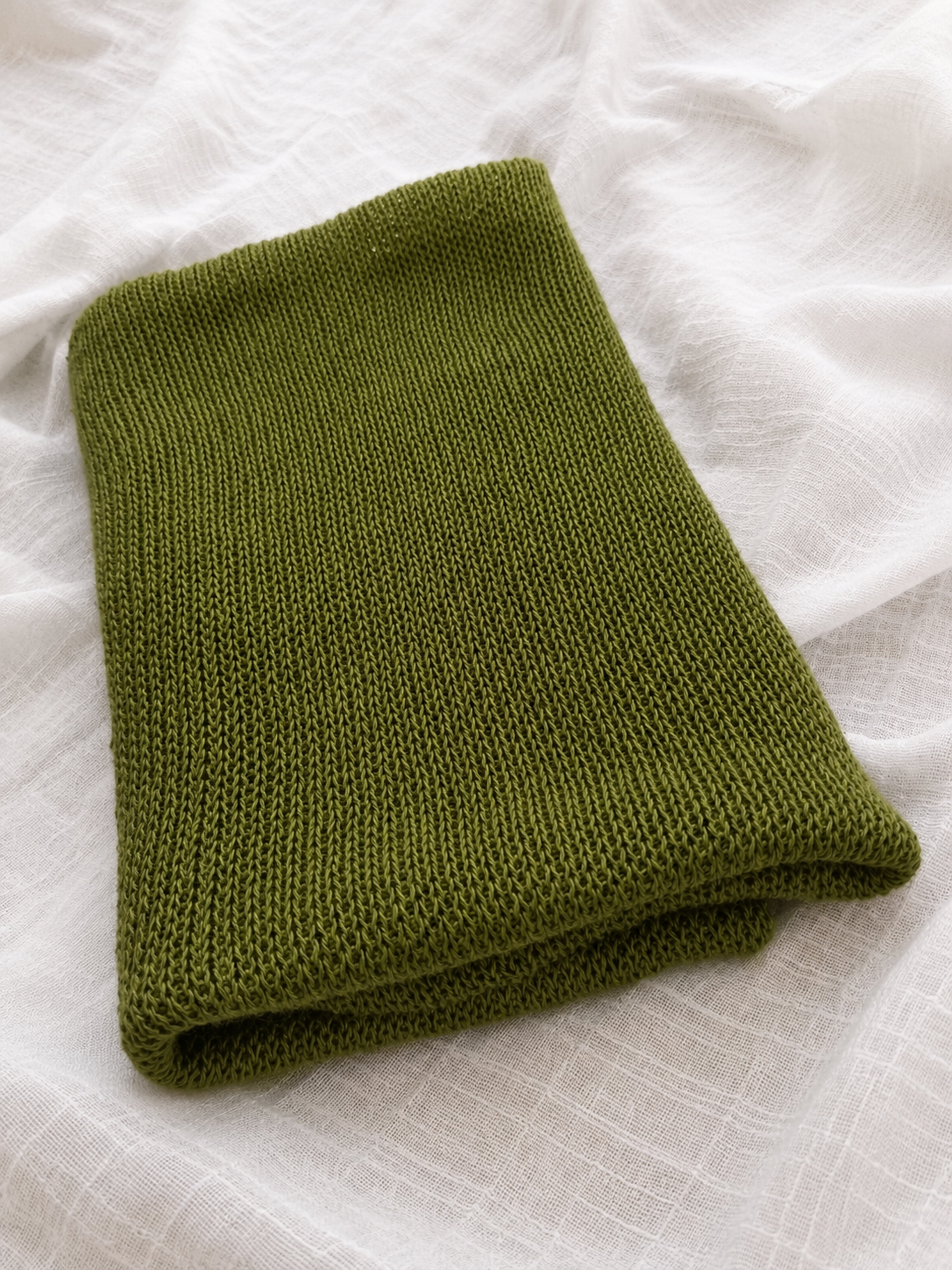 Folded Olive Green linen infinity scarf on natural linen fabric.