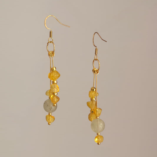 A pair of gold drop earrings featuring textured irregular yellow baltic amber beads detailed with round green grey prehnite gemstone