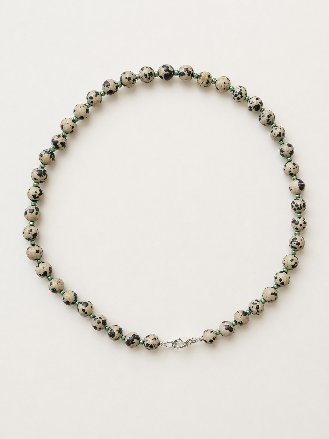 Dalmatian jasper necklace with green accents and silver-colour lobster clasp on a warm ivory background