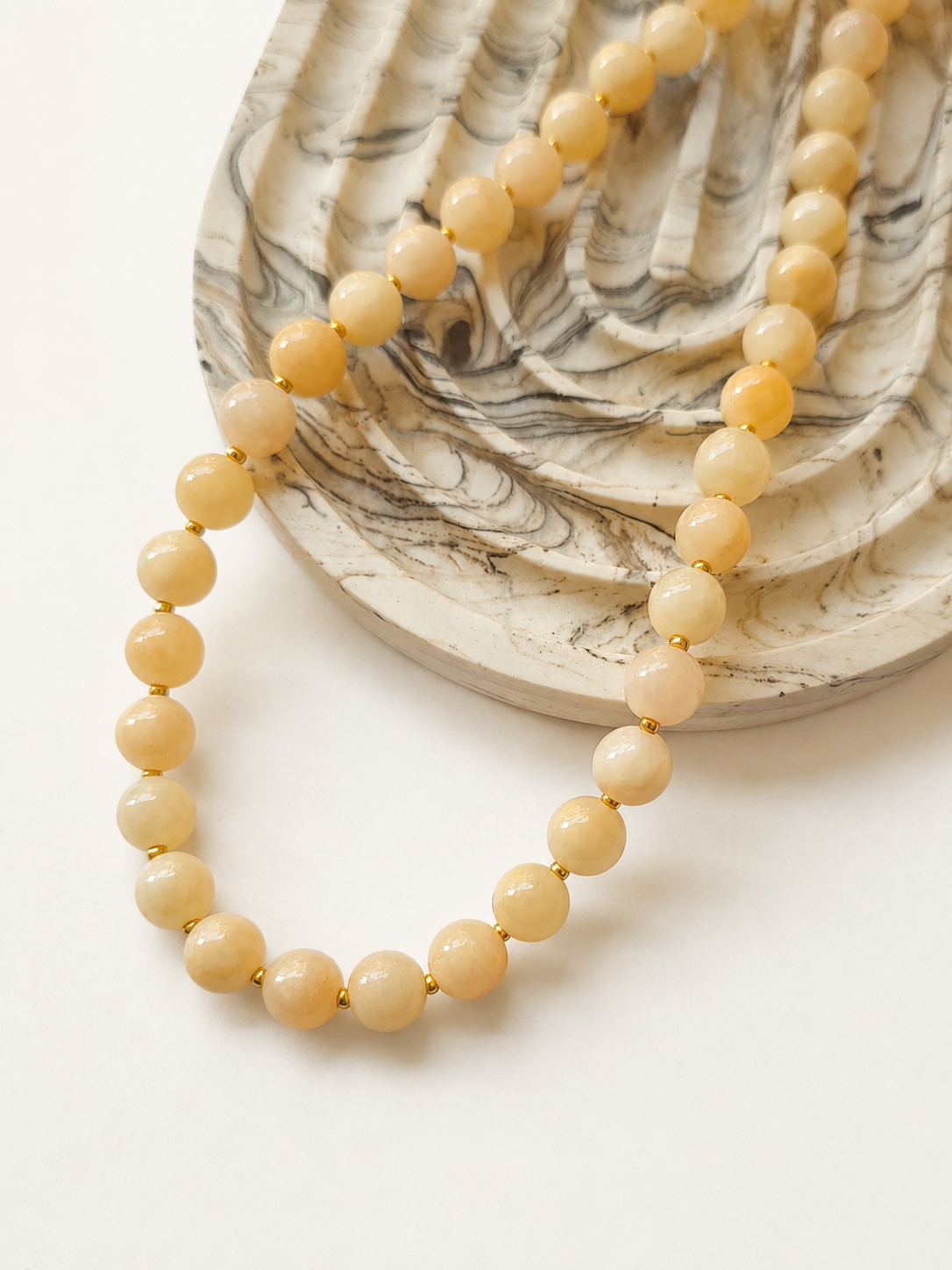 Light peach jadeite necklace arranged around a marble dish in a lifestyle composition