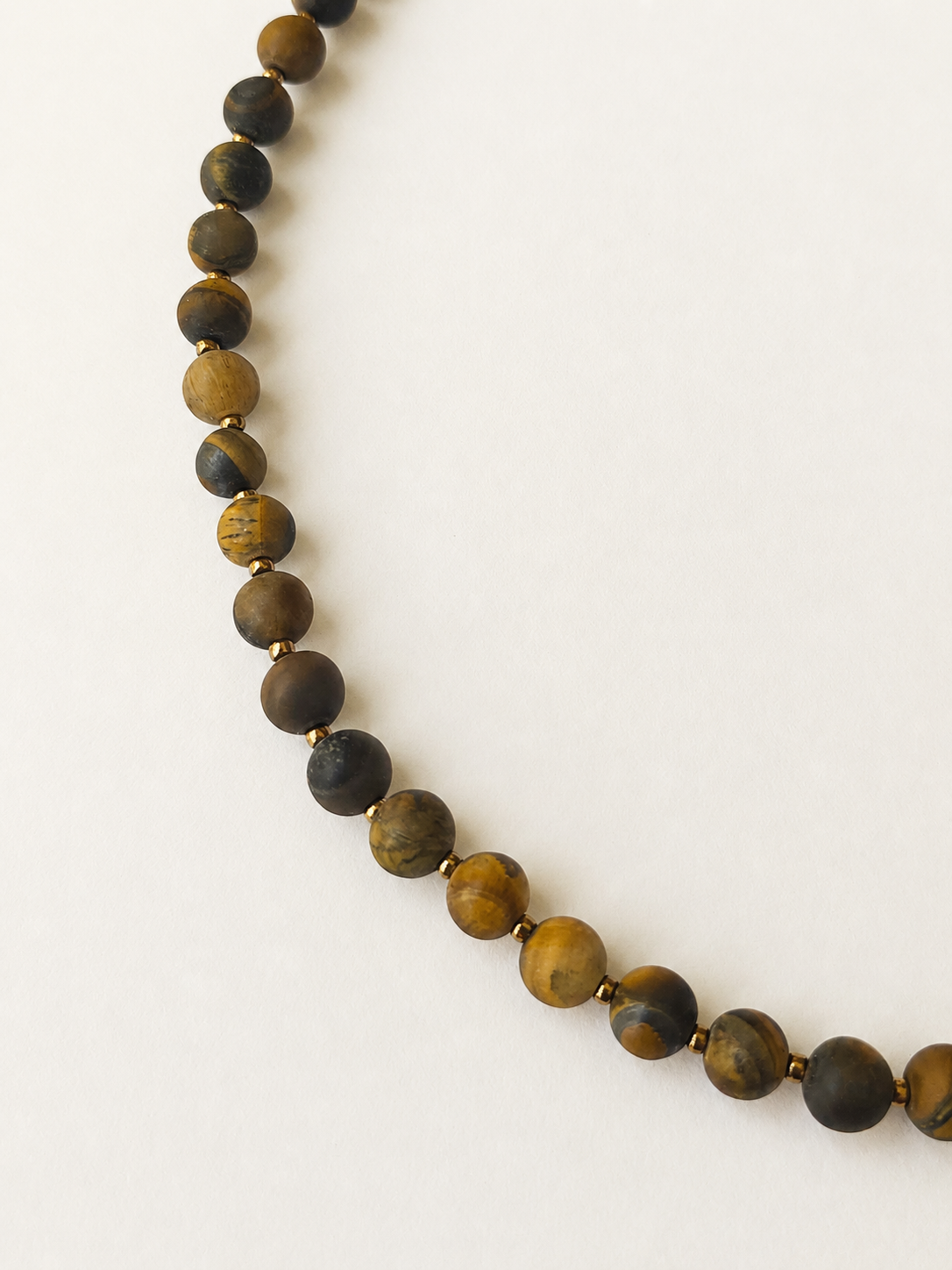 Close-up of matte tiger eye beads with brown, golden and charcoal banding separated by gold Miyuki accents