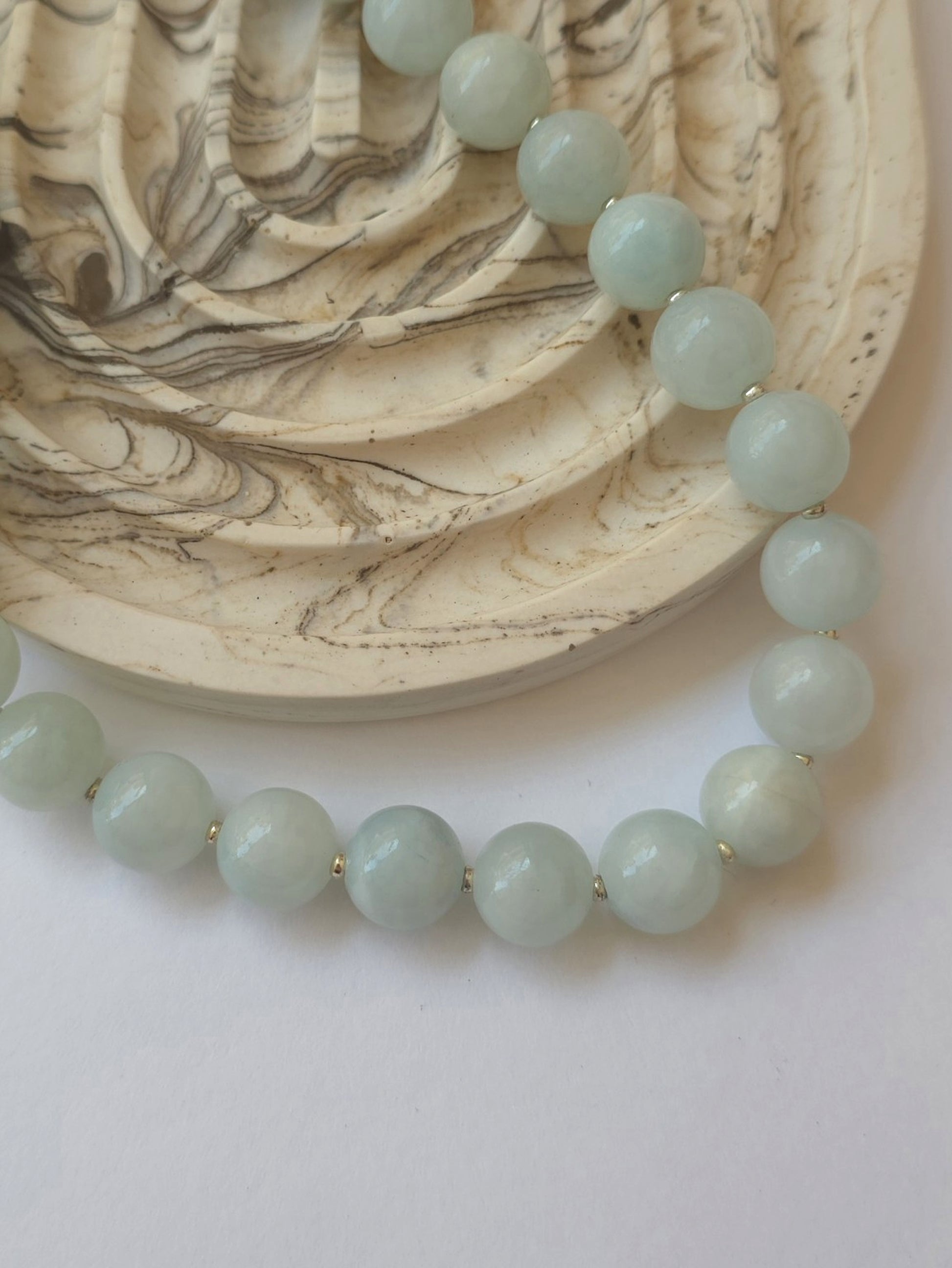 Pale green jadeite necklace styled beside a marble dish on a neutral background
