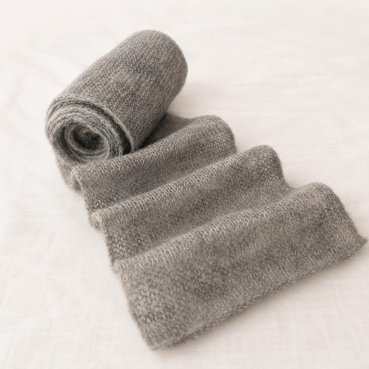 Rolled cloud grey kid mohair scarf highlighting its lightweight knit.