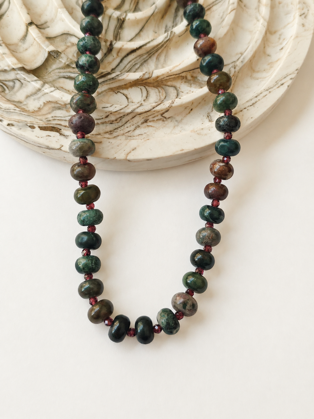 Indian agate necklace with burgundy accents styled beside a marbled neutral dish