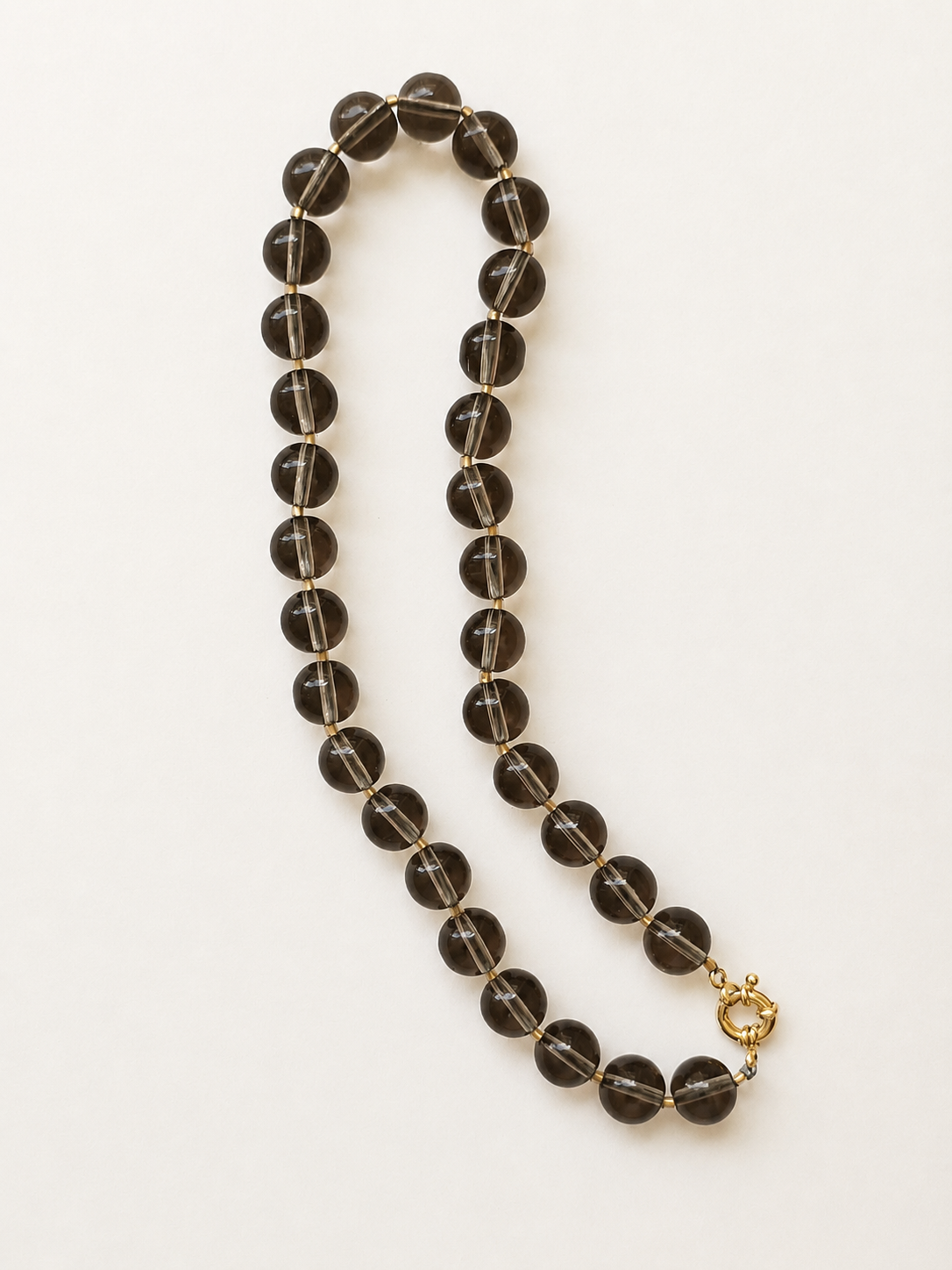 Full smoky quartz gemstone necklace arranged lengthwise on a warm ivory background