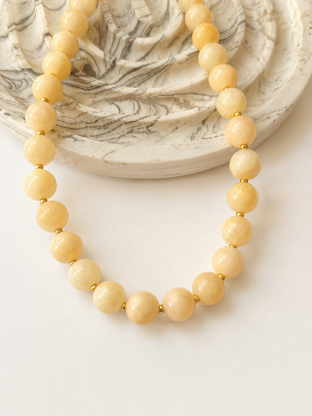 Light peach jadeite necklace styled beside a marble dish on a warm neutral background