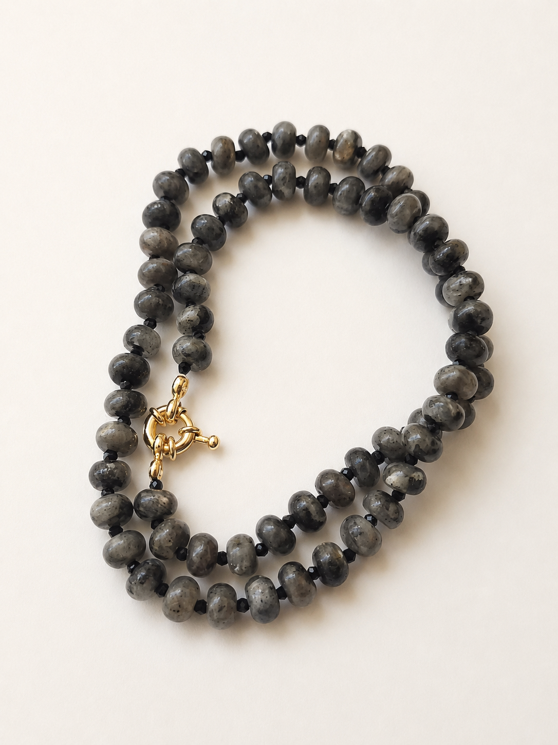Coiled labradorite necklace showing varied grey stones, black spinel accents and golden clasp
