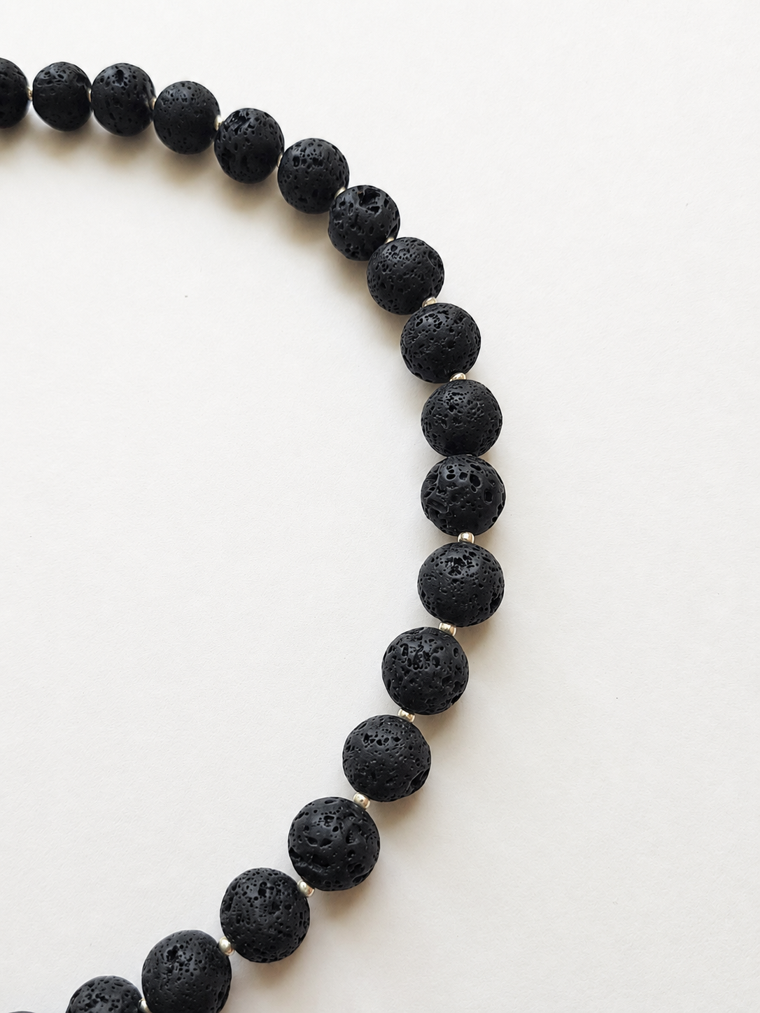 Close-up of porous 10mm black lava stones separated by silver-toned spacer beads