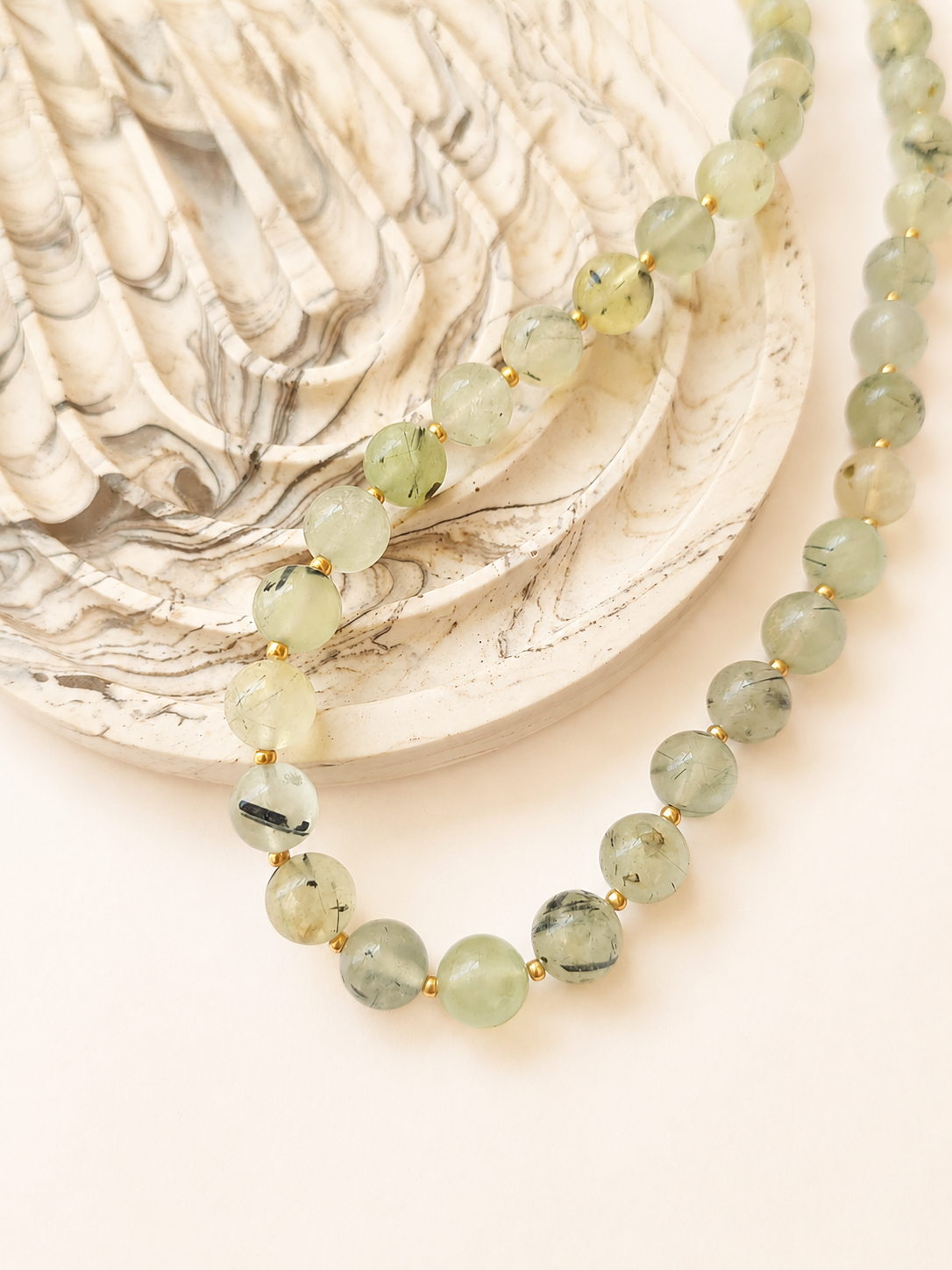 Prehnite necklace styled beside a neutral marbled decorative object