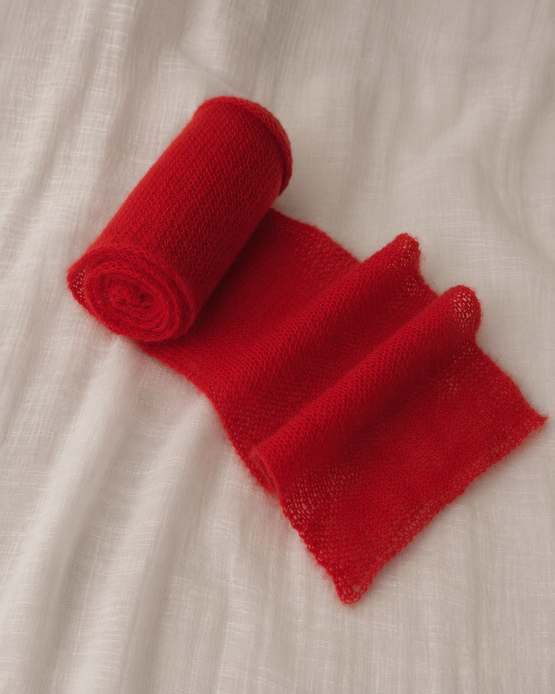Rolled Ruby Red kid mohair scarf highlighting its lightweight knit.