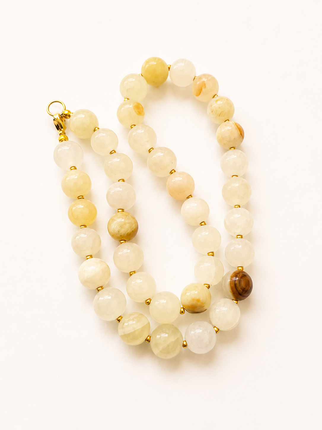 Loosely coiled cream yellow jadeite necklace with varied gemstone patterns and golden clasp