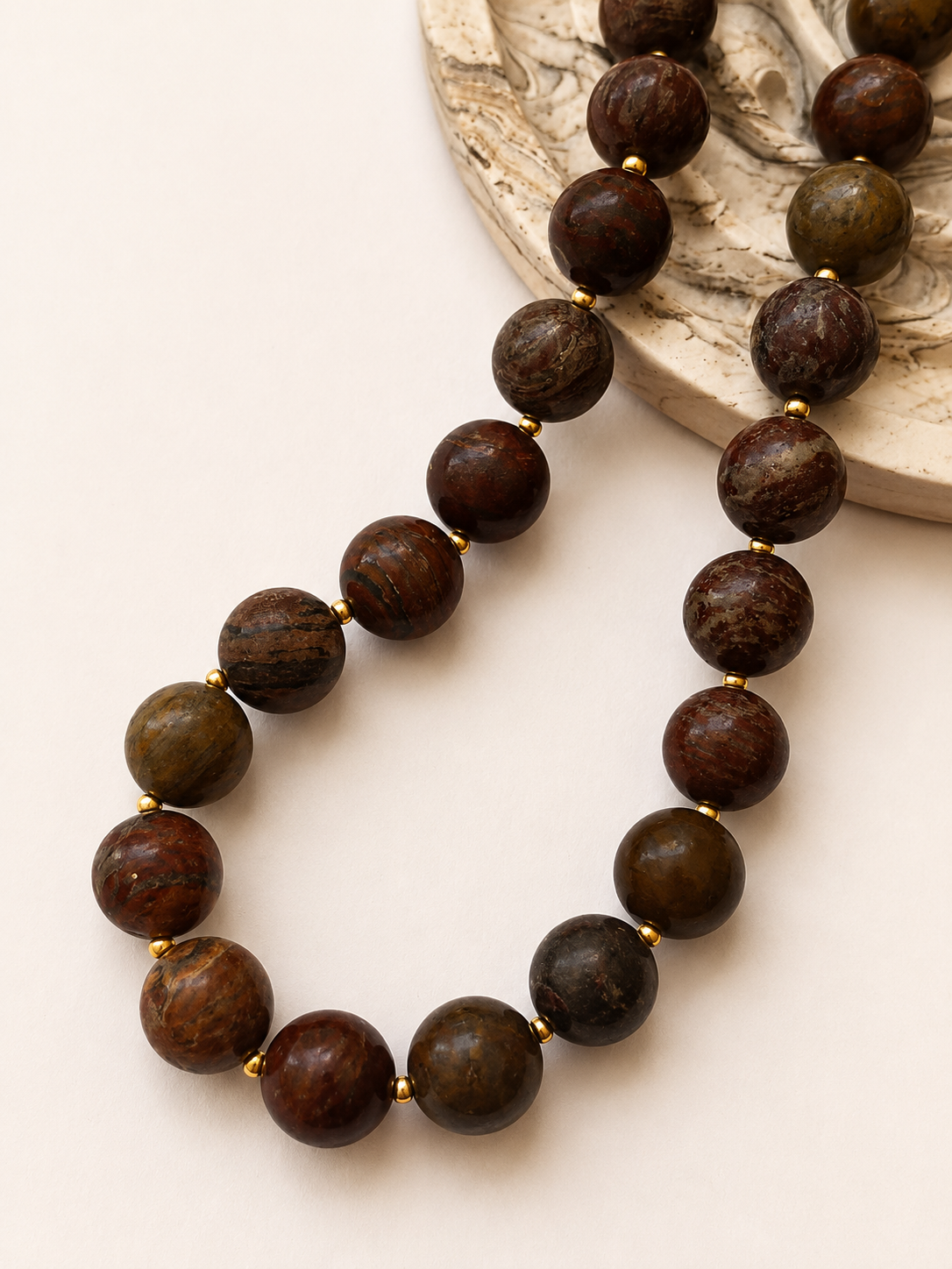 Earth-toned agate gemstone necklace styled beside a marbled decorative object