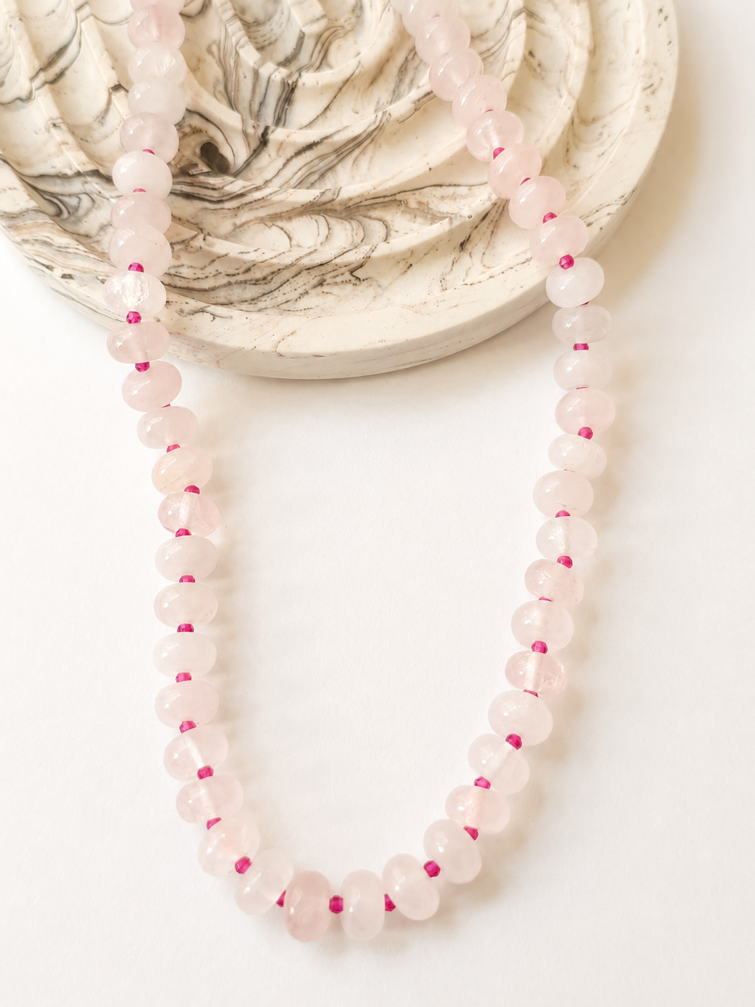 Rose quartz rondelle necklace styled beside a marble dish on a warm neutral background