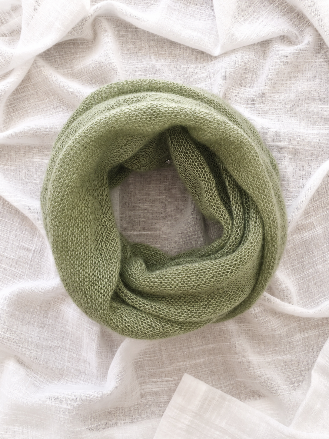 Rolled Soft Sage infinity loop scarf on white linen.