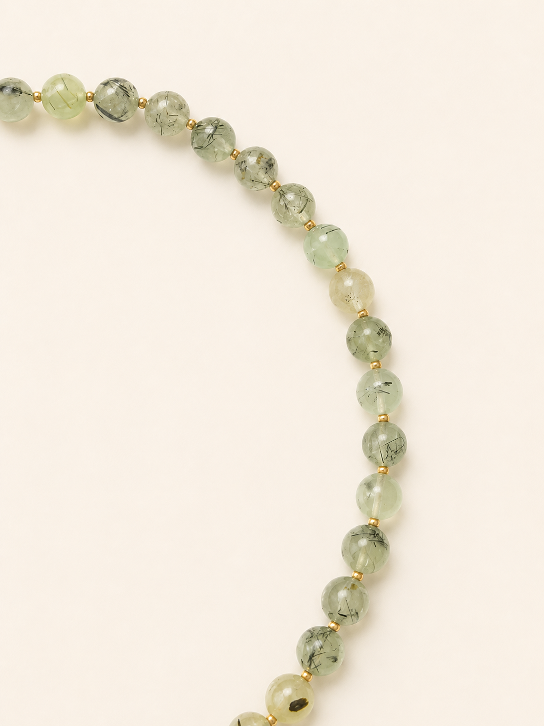 Close-up of pale green prehnite beads with dark natural inclusions and gold Miyuki spacers